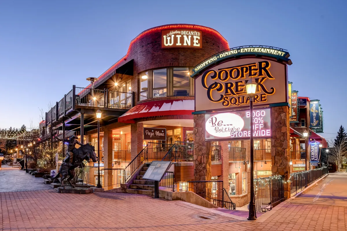 This exterior image captures the vibrant entrance to Cooper Creek Square, featuring its prominent signage, decorative lighting, and visual cues of shops and dining areas. The scene is lively and bustling, hinting at the heart of downtown activity and the accessibility of multiple attractions just steps away.