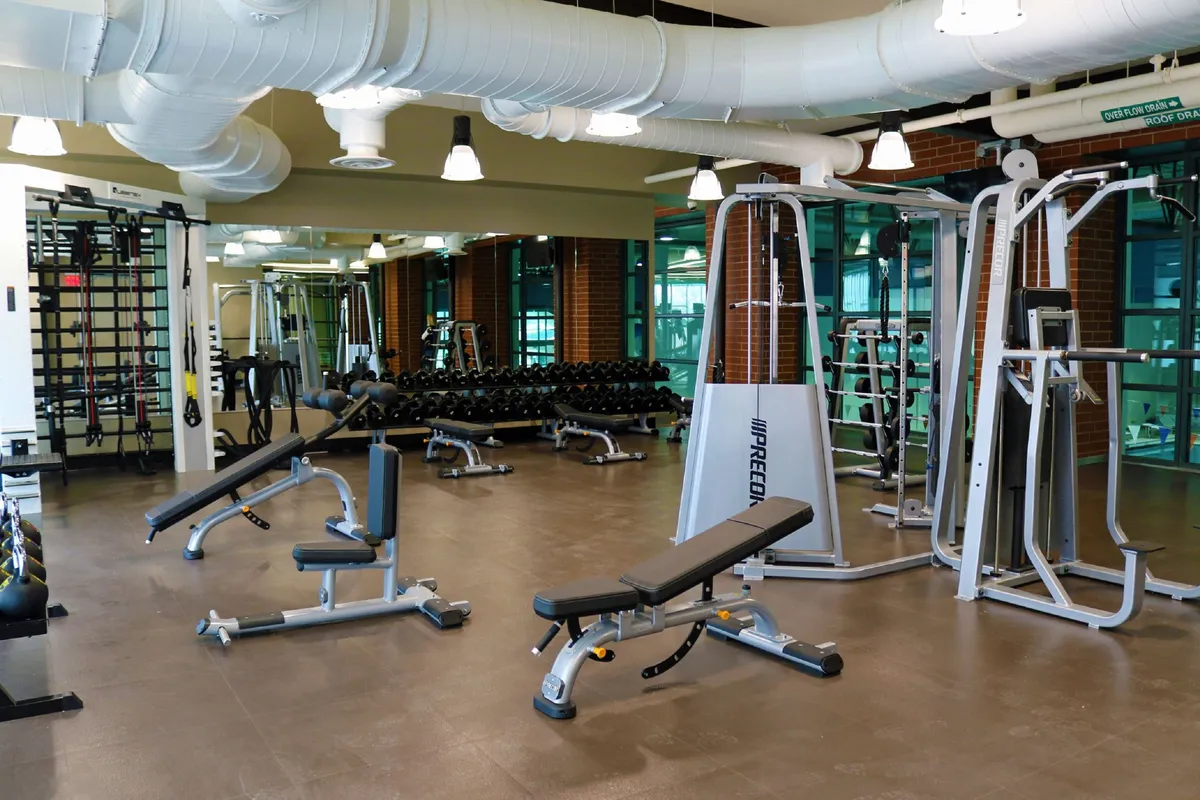 A bright and motivational fitness center equipped with weightlifting and cardio machines, mirrored walls, and dumbbell racks. The open space suggests active lifestyles and group fitness activities, resonating with community engagement.