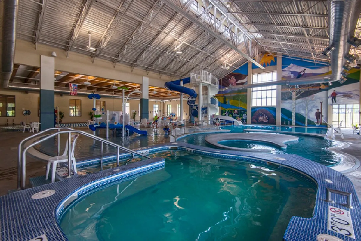 An energetic interior shot of an indoor swimming pool and colorful water slides, with children playing and families enjoying the recreational atmosphere. Bright murals bring vibrancy to the space.