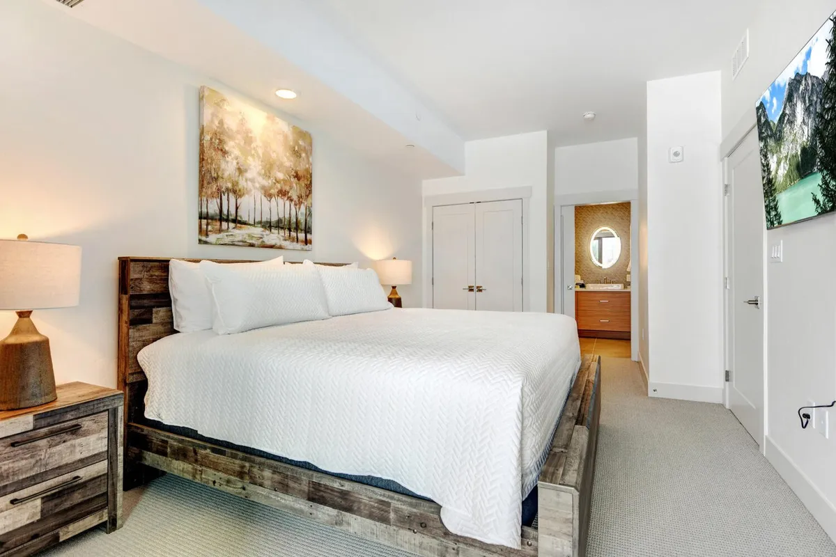 A tranquil bedroom featuring a king-sized bed with plush bedding, soothing artwork above the headboard, and nightstands with lamps to each side. Soft natural light filters through windows, creating a serene and restful atmosphere ideal for unwinding after a day of adventure.