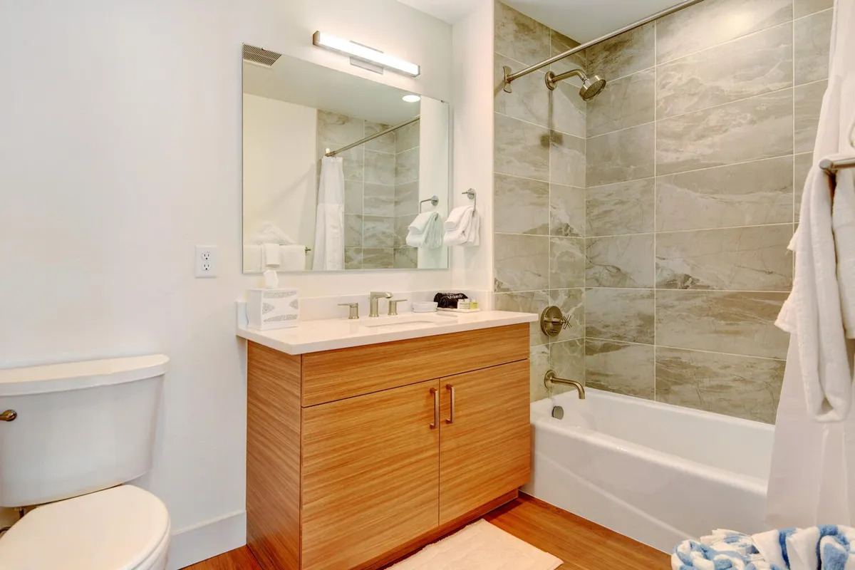A bright, spa-like bathroom featuring a wooden vanity, a marble shower wall, and a large mirror. The setting feels inviting and refreshing, perfect for self-care and relaxation with hotel-grade toiletries.