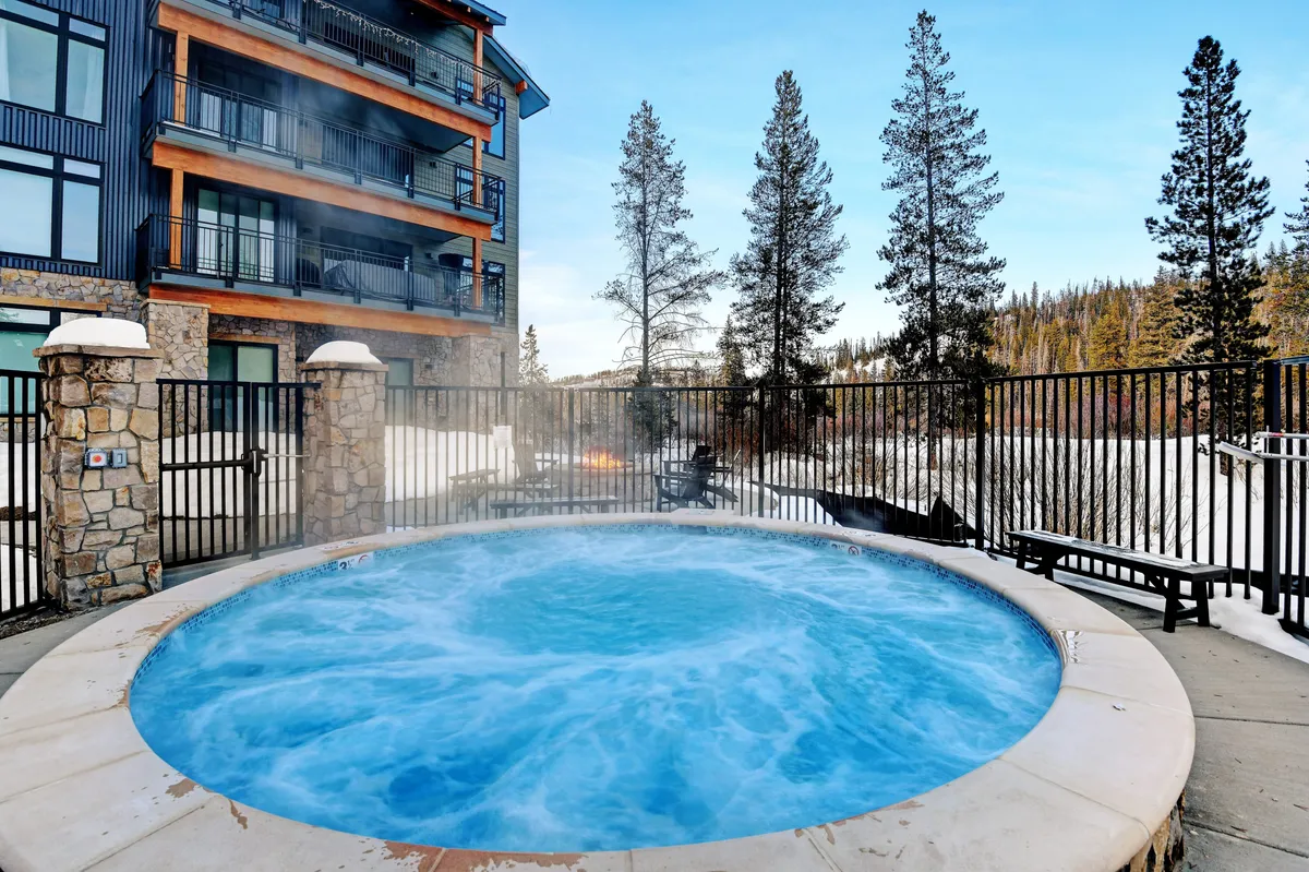 An inviting outdoor hot tub set among trees, with a glimpse of the building exterior in the background. The scene feels tranquil, suggesting relaxation after a day of exploration or adventure, with possibilities for stargazing and socializing.