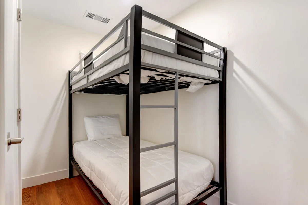 A practical and inviting bunk room with twin-over-twin beds featuring crisp white bedding and a warm wood floor. The space is designed with kids or extra guests in mind, offering a playful yet restful setting.