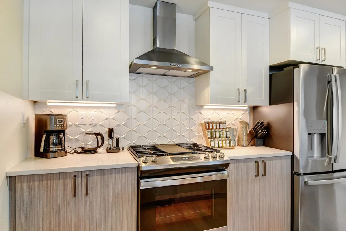 A stylish kitchen with stainless steel appliances, a geometric tile backsplash, a coffee maker on the counter, and modern wood cabinetry. The overall mood is inviting and practical, blending upscale touches with everyday functionality.