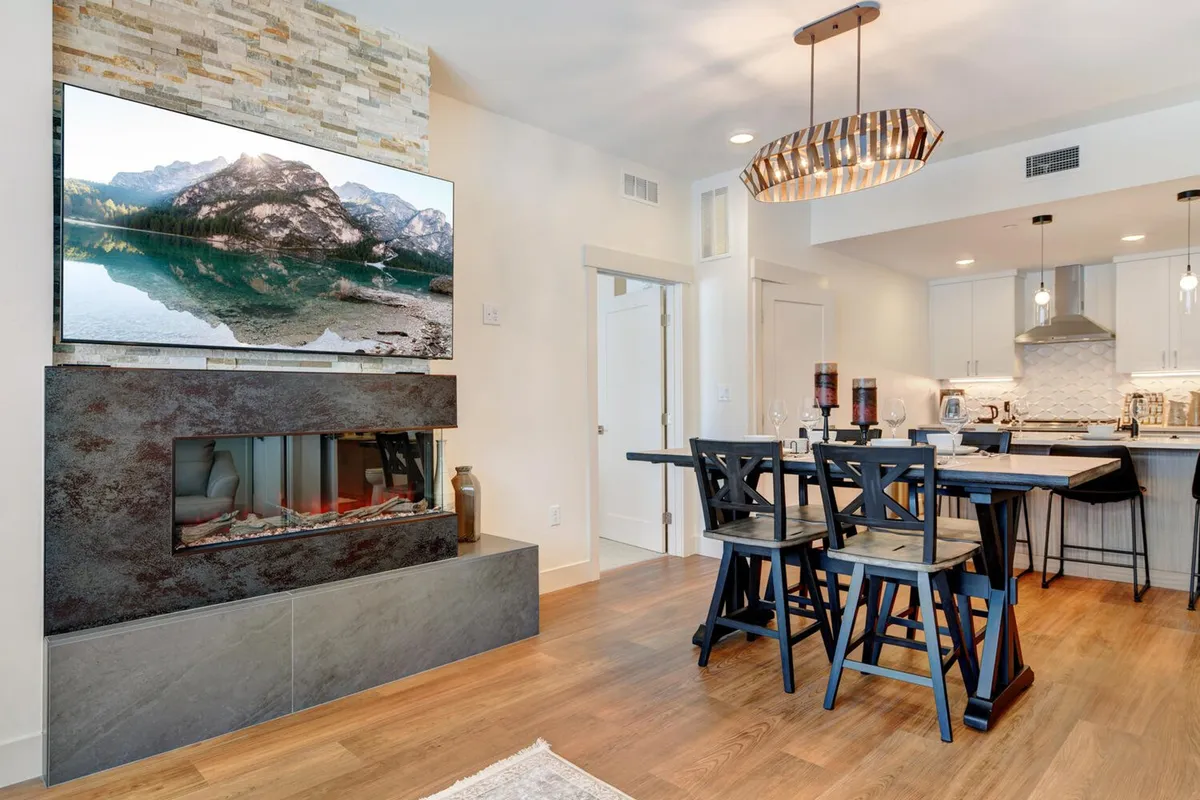 A cozy gathering space featuring a fireplace, a dining table set for multiple people, and a television. The room is warmly lit and invites both intimate dinners and group socializing, with large windows that might hint at a connection to the downtown atmosphere outside.