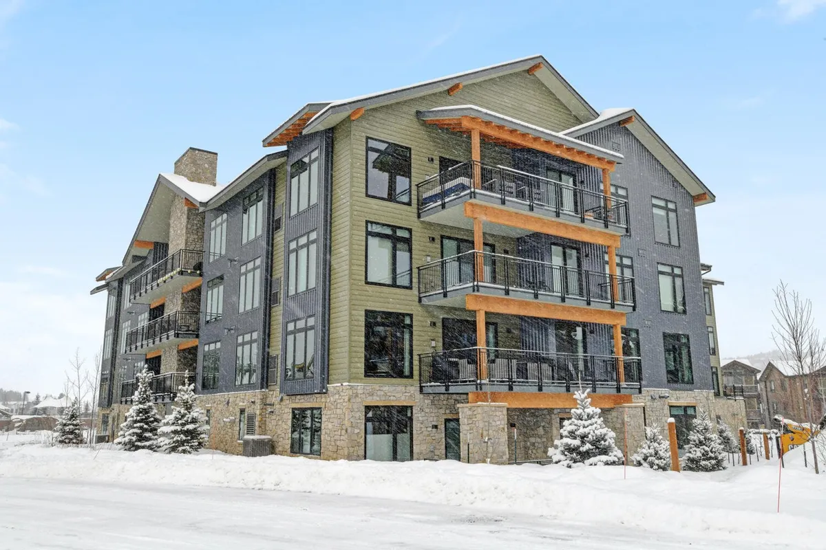 A beautiful exterior shot with modern architecture featuring stone facades and balconies, with snow covering the ground. People are visible skiing, snowboarding, and relaxing on balconies, evoking a festive, cozy winter atmosphere.