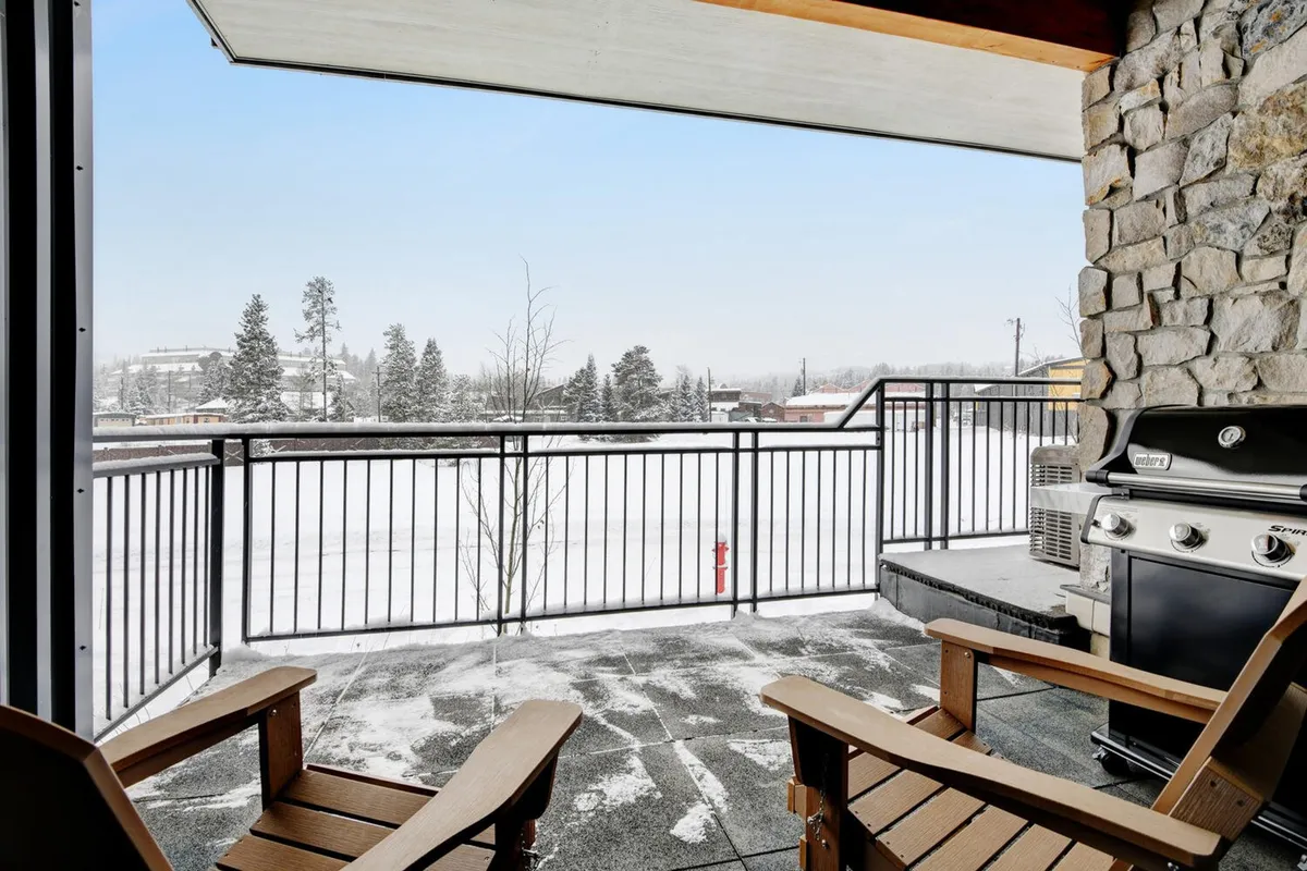 A serene winter exterior featuring wooden chairs and a grill on a snow-covered patio. The scene invites guests to relax outdoors, enjoy mountain views, or share stories after a day of adventure.