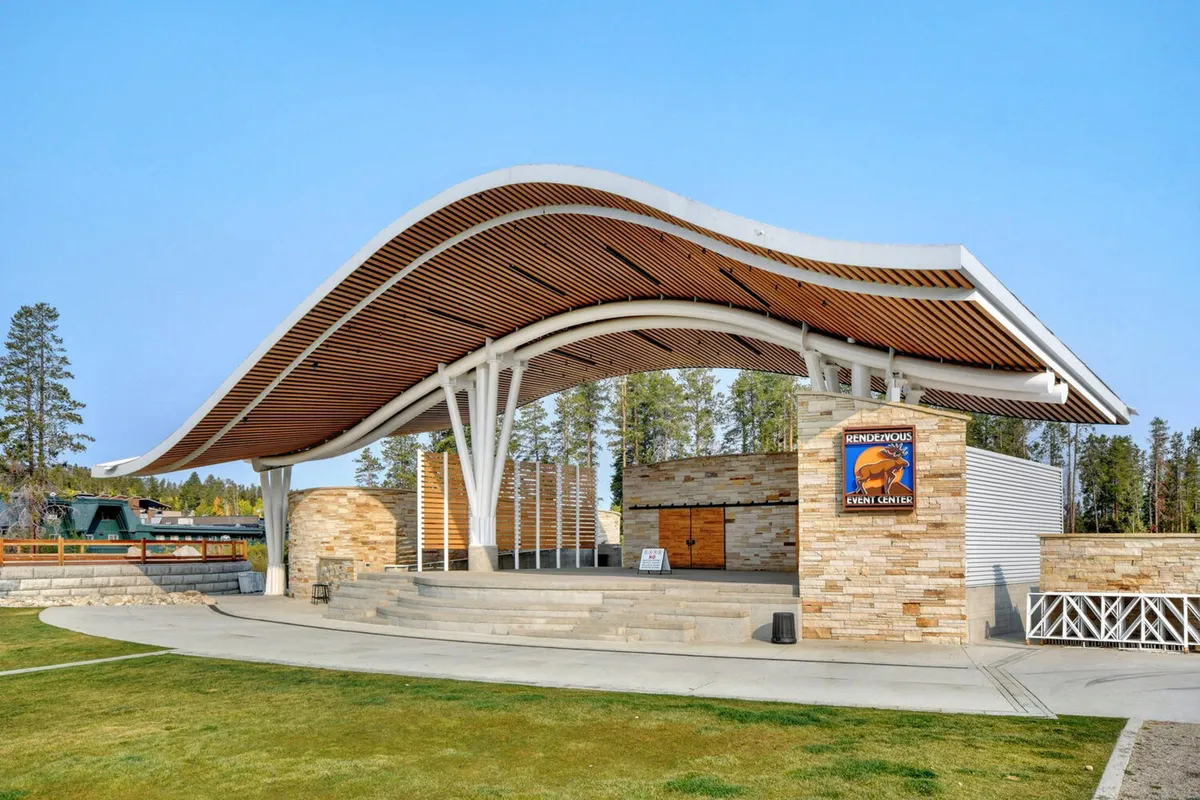 The photo showcases Hideaway Park’s unique amphitheater, with its curved roof structure, stone wall accents, and open stage area set for outdoor performances and community gatherings. The festive energy suggests an inviting space for live music and family-friendly events.